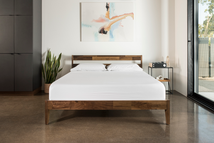 Picture of a Tuft & Needle mattress and wood bed frame sitting in a room with a picture hanging above the bed
