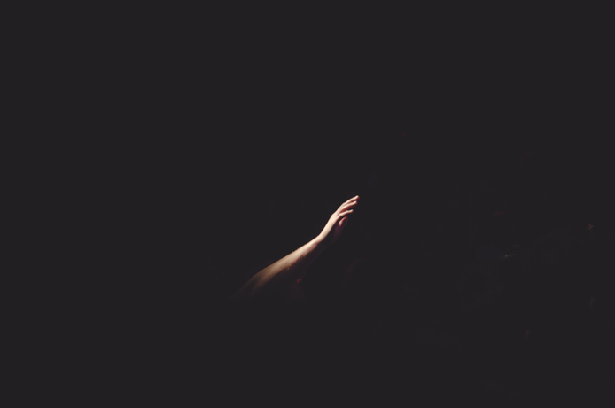 Half of an arm reaching up out of a black background