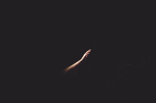 Half of an arm reaching up out of a black background
