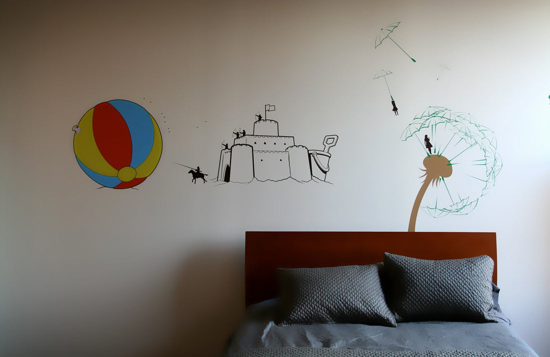 A mural of a beach ball, sand castle and dandelion on the wall above a bed