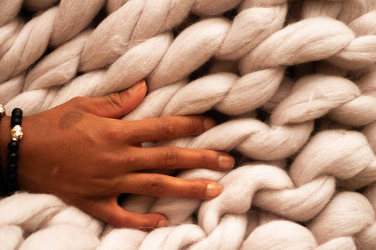 A hand gently resting on a pile of white wool weaved together