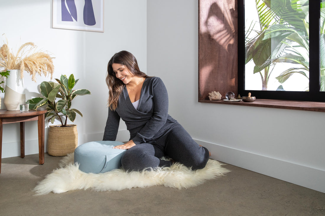 Woman sitting on a white fluffy run next to a Tuft and Needle meditation cushion