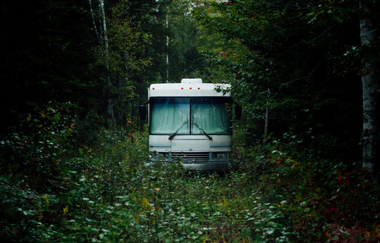 Picture of the front of an RV sitting in a grassy meadow surrounded by trees