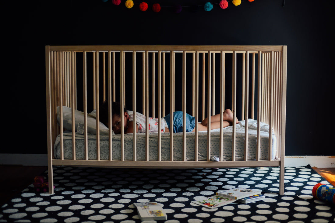 Picture of a toddler sleeping in a light wood crib on their stomach