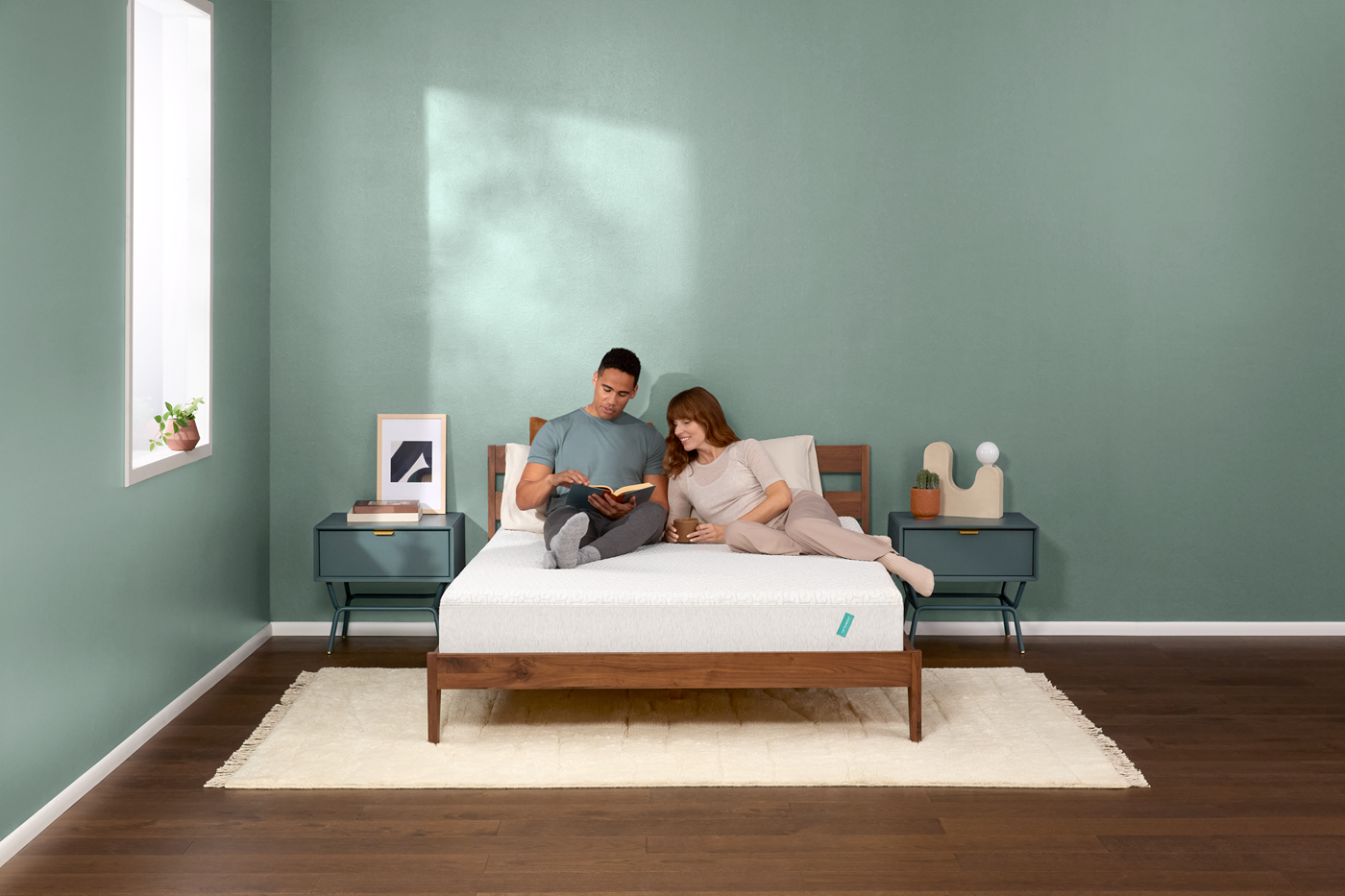 A man and a woman are shown on a Tuft and Needle Mint Hybrid mattress in a bedroom setting with a circular 'Forbes Best Product Awards' badge on the right side.