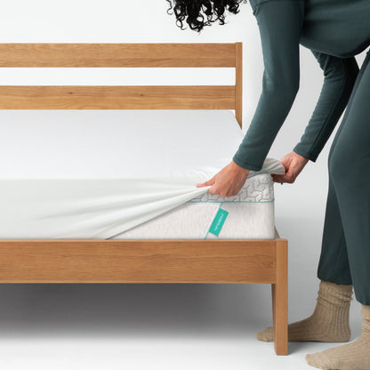 Woman placing a mattress cover on top of a Tuft and needle mattress placed in a brown bed frame