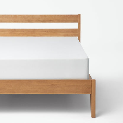 Tuft and needle mattress placed in a brown bed frame with a mattress cover on the mattress