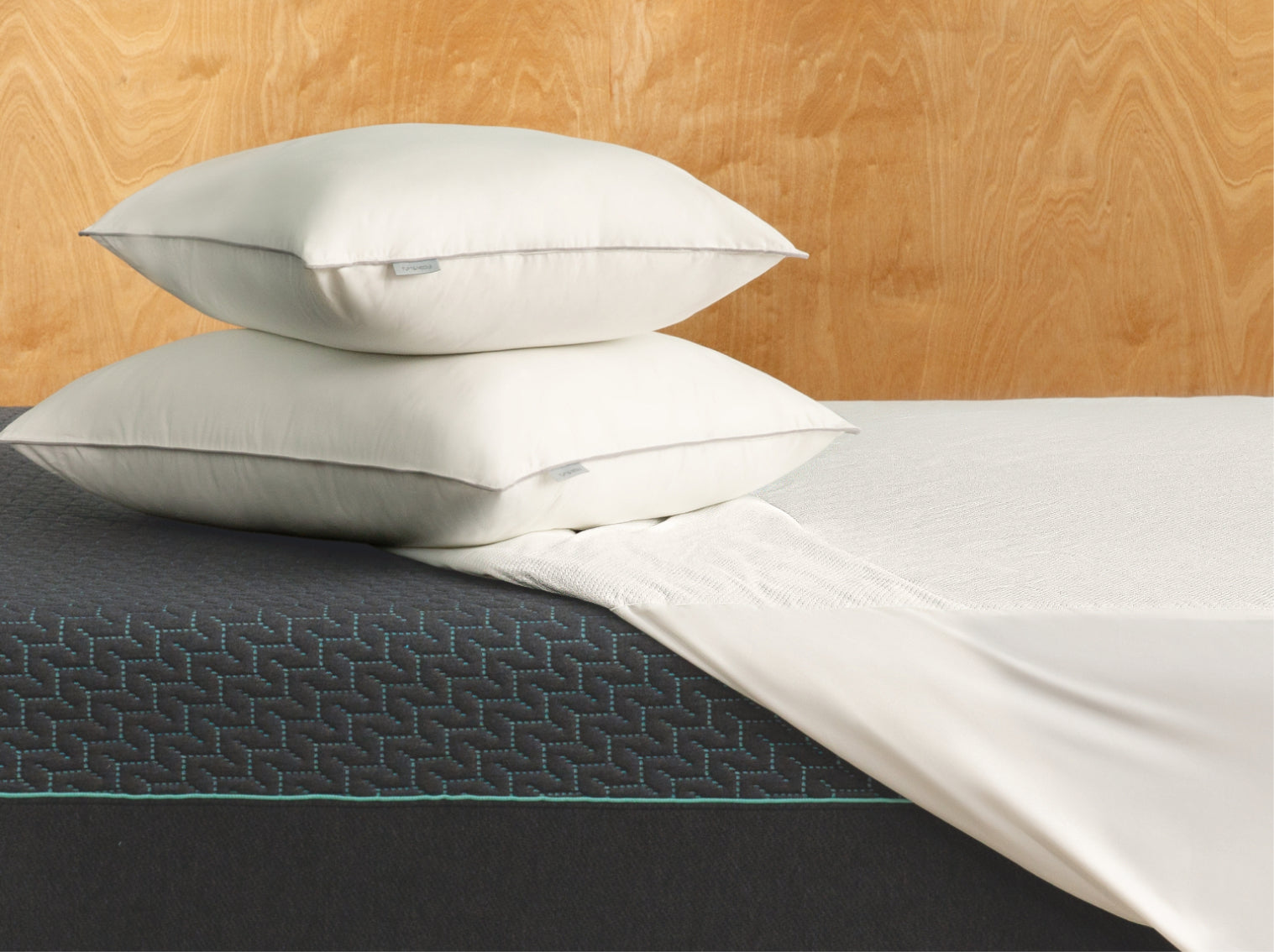 Two Tuft and Needle white pillows on a Tuft and Needle mint mattress with a wooden headboard.