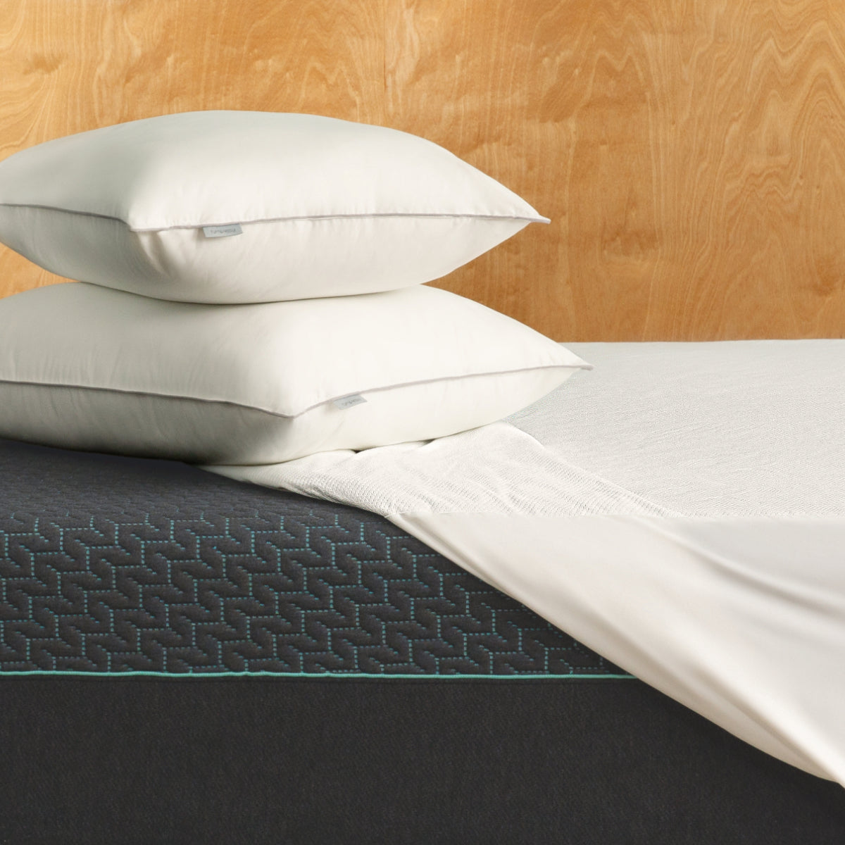 Stack of Tuft and Needle white pillows on a Tuft and Needle Mint mattress with a wooden headboard