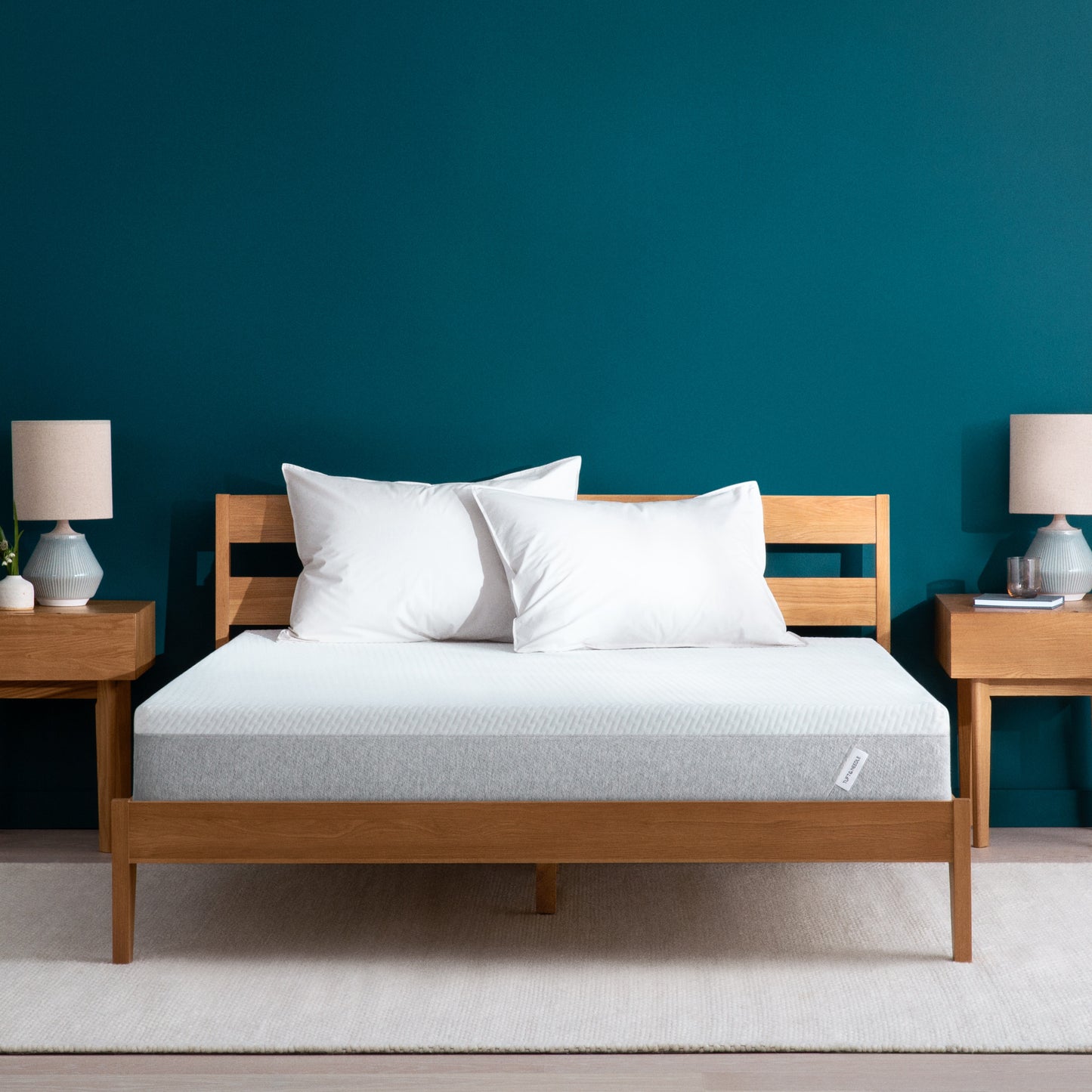 Tuft and Needle Original mattress sitting in a wooden bed frame with two pillows on top of it.