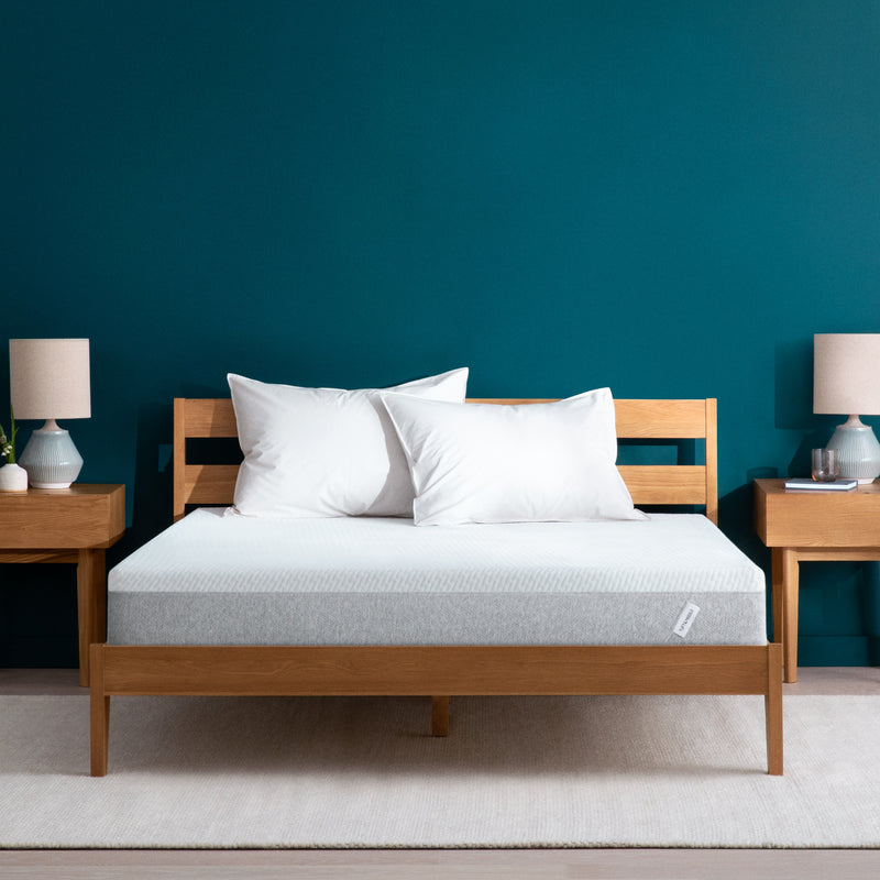 Tuft and Needle Original mattress sitting in a wooden bed frame with two pillows on top of it.