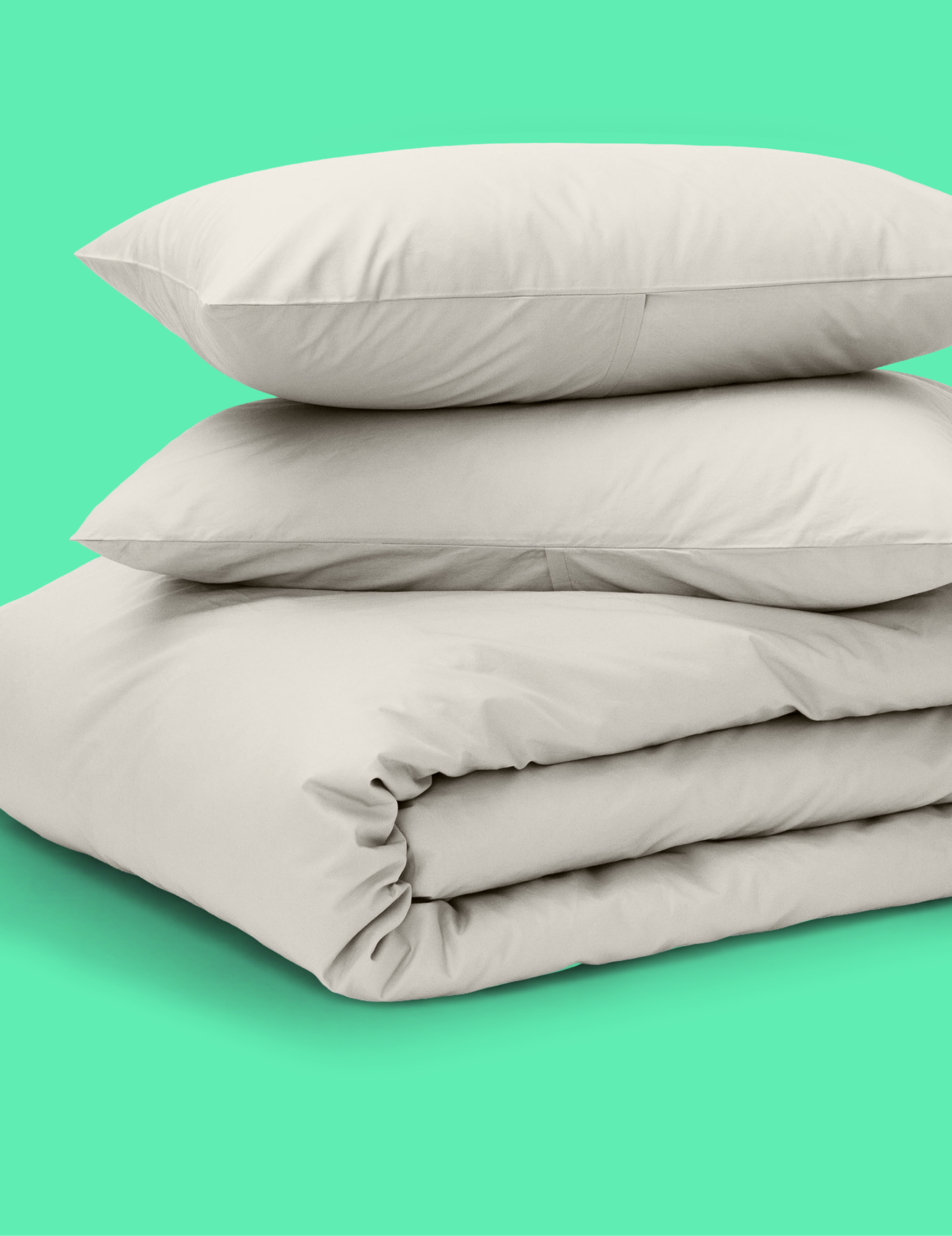 A stack of light beige Tuft and Needle bedding, including two pillows and a folded duvet cover, set against a solid mint green background.