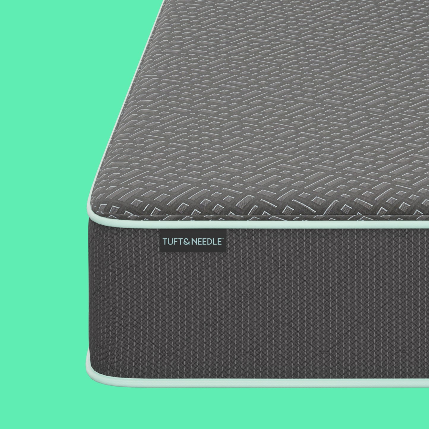 Close-up corner view of a the Tuft and Needle  13.5" Mint Hybrid II mattress showing a dark gray textured top surface and side panel with a visible TUFT & NEEDLE label, set against a solid mint green background.