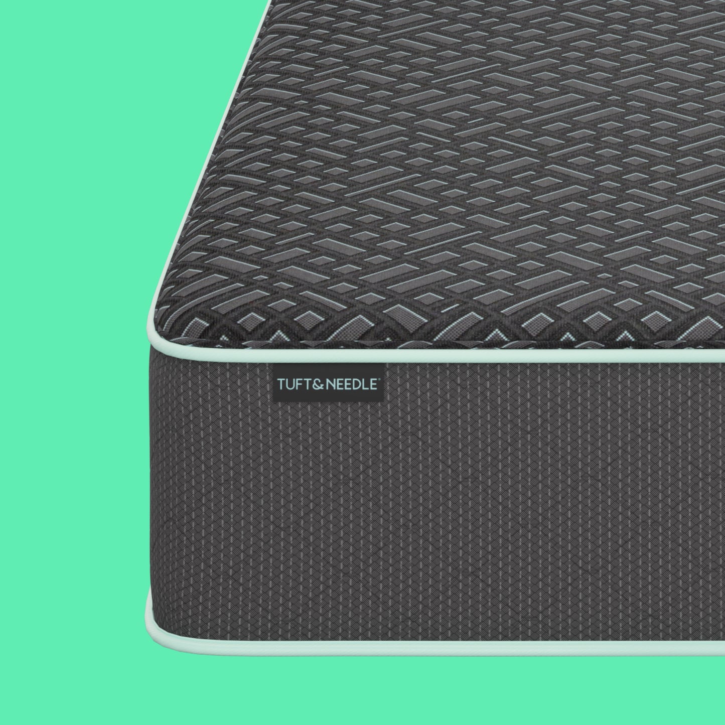 Close-up corner view of a the Tuft and Needle 15 inch Mint Luxe Hybrid Plush mattress showing the dark textured top surface and side panel with a visible TUFT & NEEDLE label, set against a solid mint green background.