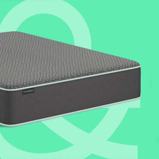 A dark gray Tuft & Needle 14 inch Mint Hybrid mattress II shown at an angle against a mint green background with abstract light green shapes. The brand name Tuft & Needle is visible on a small label on the side of the mattress.