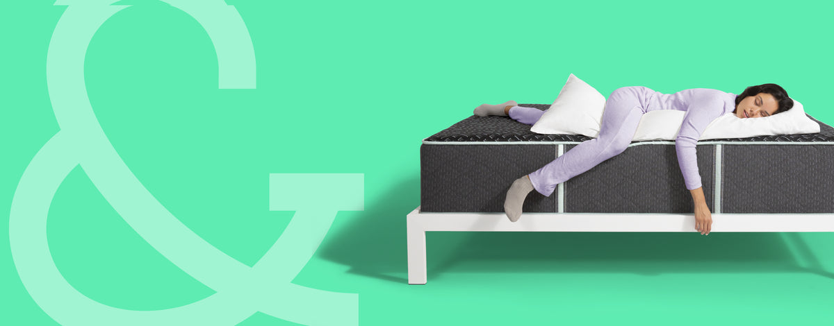 Woman laying on top of a Tuft and Needle Mint Hybrid lux mattress sitting on a white wood bedframe with 2 pillows on top of it.