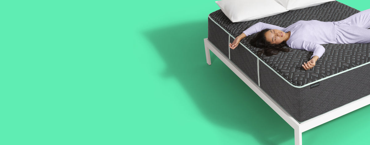 Woman laying on her back asleep on top of a Tuft and Needle mattress with 2 pillows on top of it.
