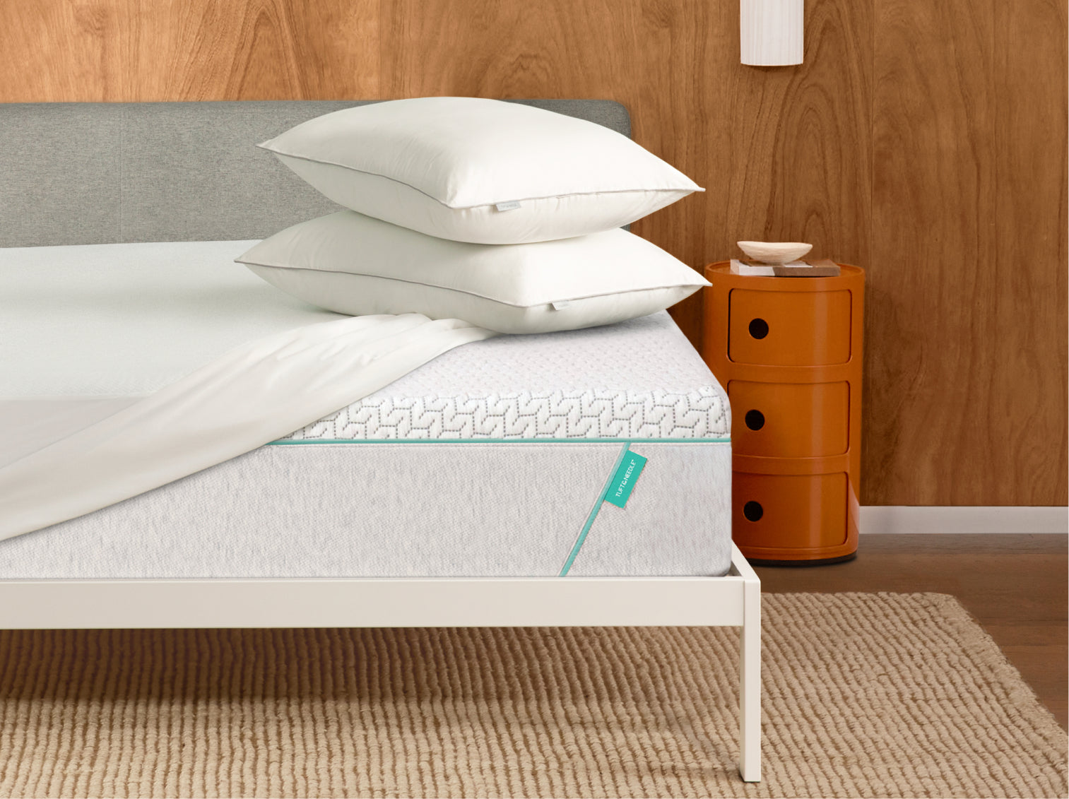 Two Tuft & Needle Foam Pillows on top of a Tuft and Needle original mattress with a mattress protector on top of it all sitting in a white bed frame.