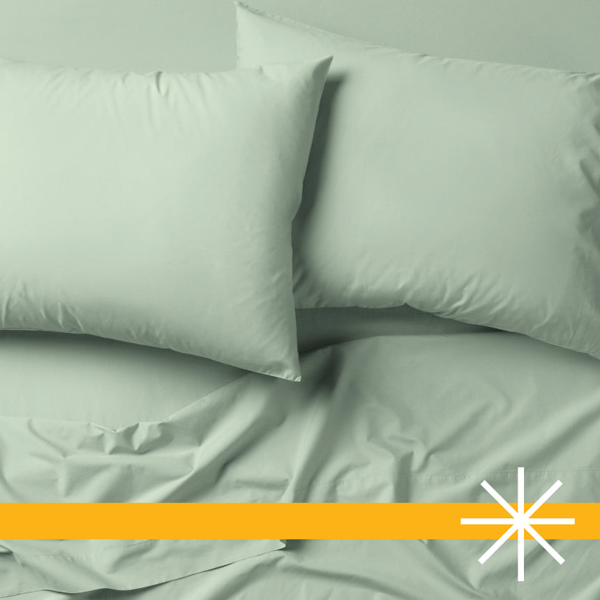 Tuft and Needle green bedding, two pillows encased in 2 green pillow cases on top of 2 sheets.