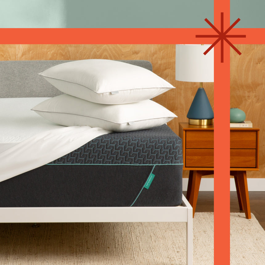 Tuft and Needle Mint Mattress sitting in a white bed frame with 2 pillows on top of it.