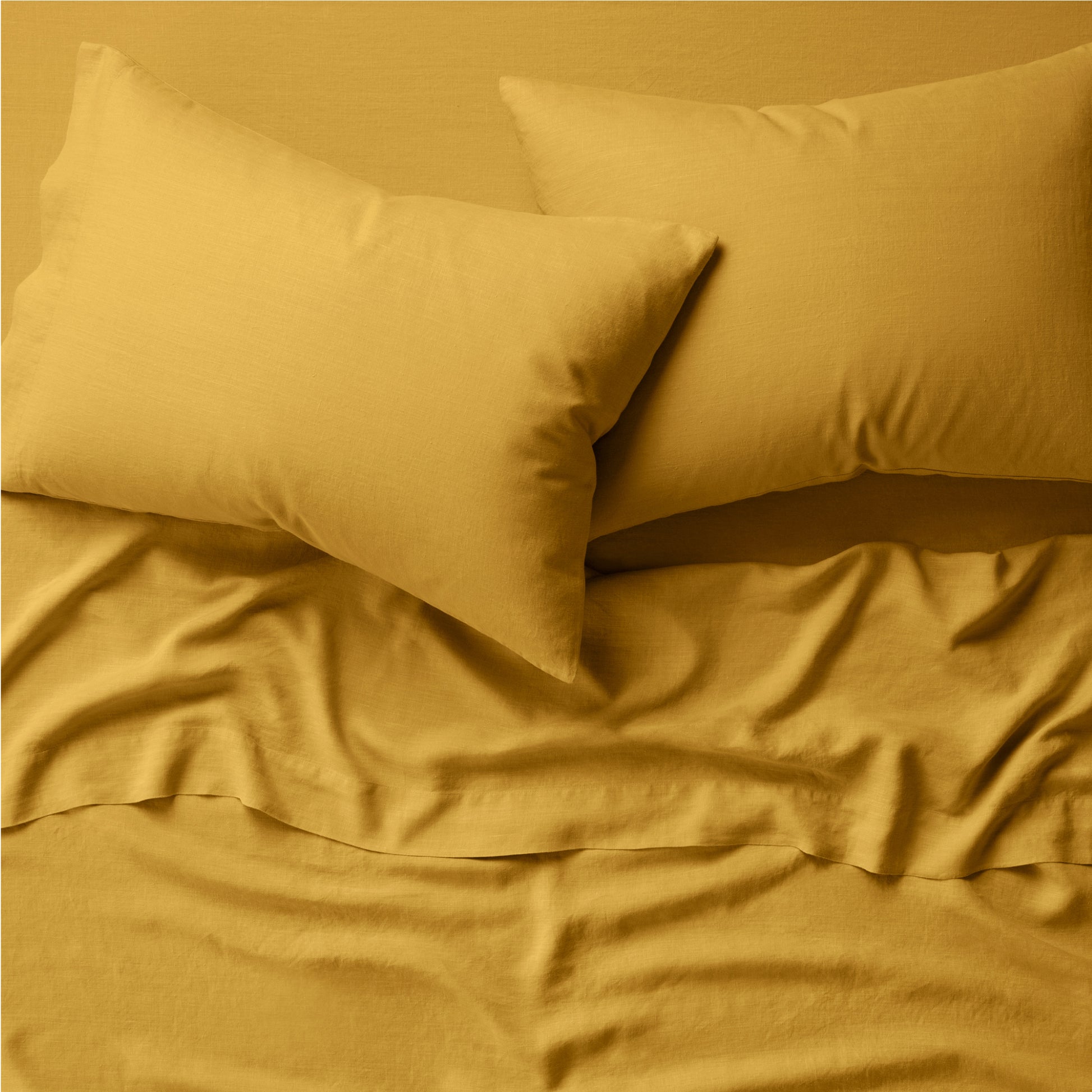 Two pillows on a bed dressed in the Tuft and Needle Hemp Pillowcase Set||color:honeycomb