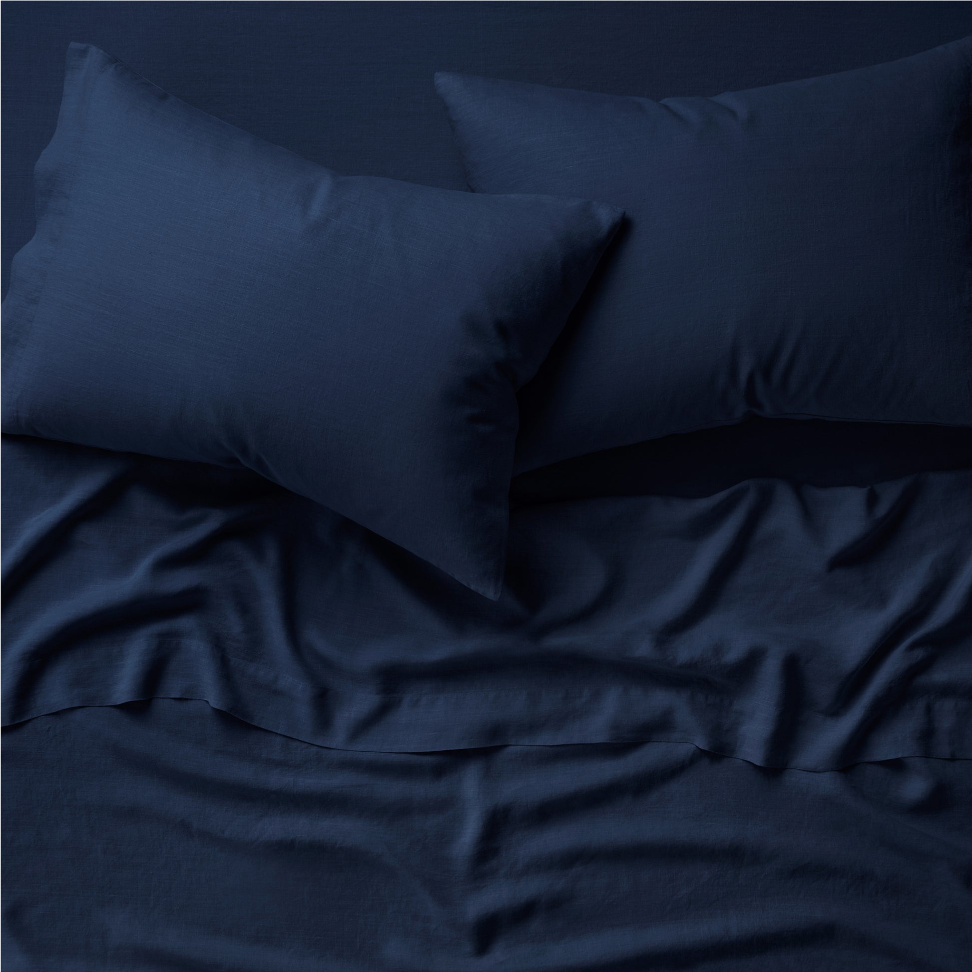 Two pillows on a bed dressed in the Tuft and Needle Hemp Pillowcase Set||color:midnight