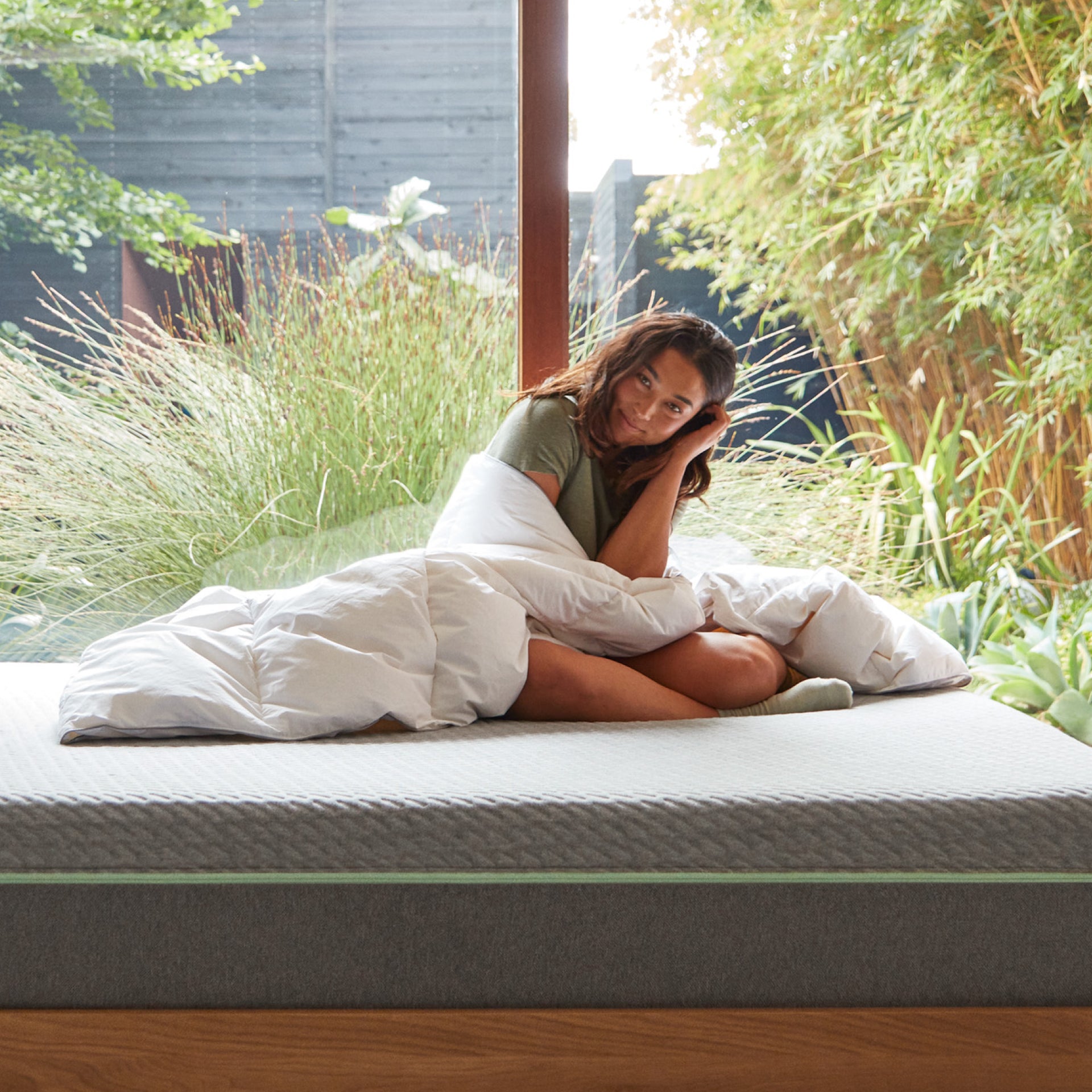 A woman sitting on a bed wrapped in the Tuft and Needle Alternative Duvet Insert||weight:medium