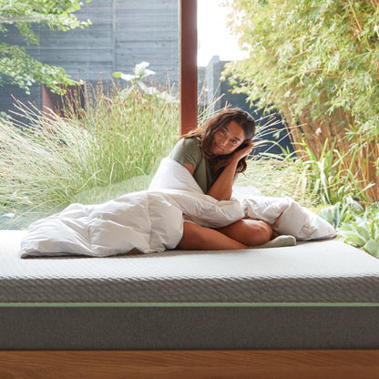 A woman sitting on a bed wrapped in the Tuft and Needle Alternative Duvet Insert||weight:medium