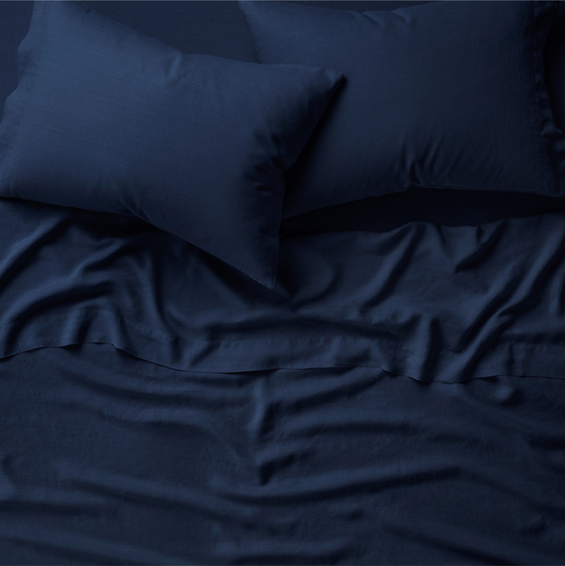 Tuft and Needle midnight sheet set on a mattress and 2 pillows on top.