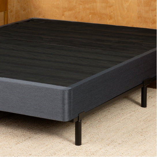 Tuft & Needle Black bed frame on a beige carpet with wooden wall in the background