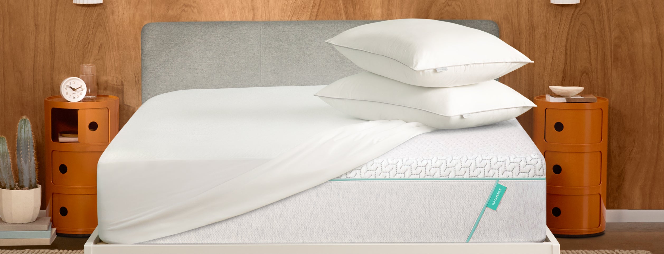 Tuft and Needle Mattress with white bedding and pillows on a wooden bed frame against a wooden wall.