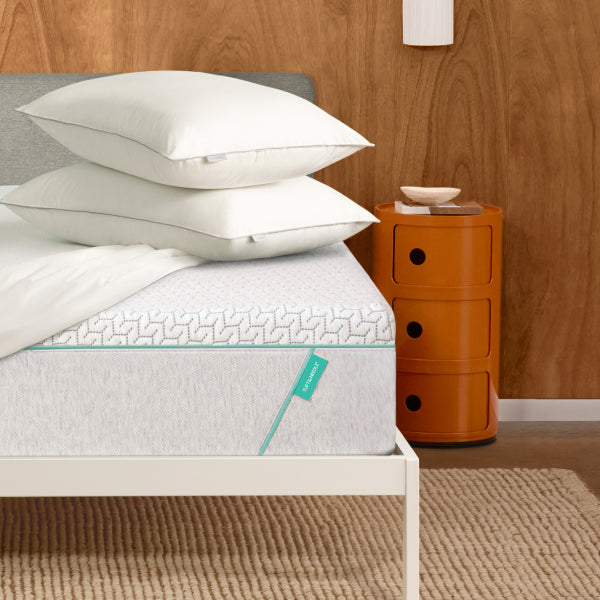 Two Tuft & Needle Foam Pillows on top of a Tuft and Needle original mattress with a mattress protector on top of it all sitting in a white bed frame.