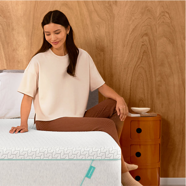 Woman sitting on a Tuft & Needle Original Hybrid mattress with her hand rubbing on the top of it.
