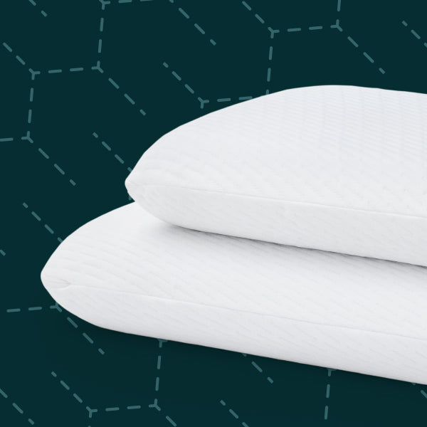 Two white Tuft and Needle pillows stacked on a dark green background with subtle geometric pattern