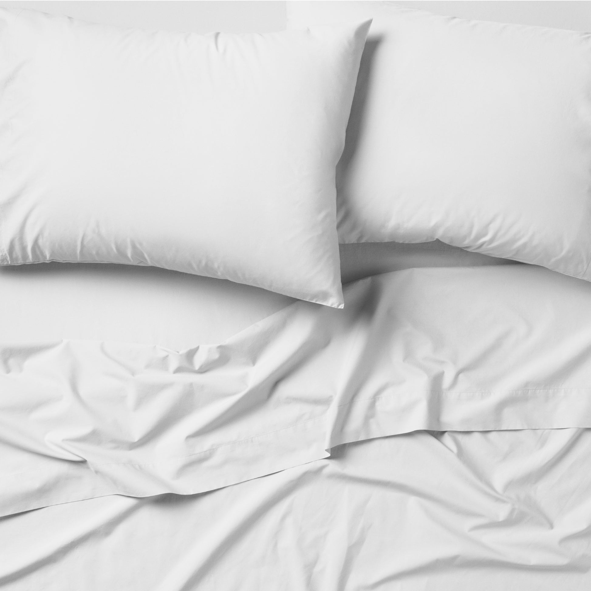 The Tuft and Needle Classic Percale Pillowcase Set, 2 pillows in a pillowcase on top of a spread out sheet || color: Cloud
