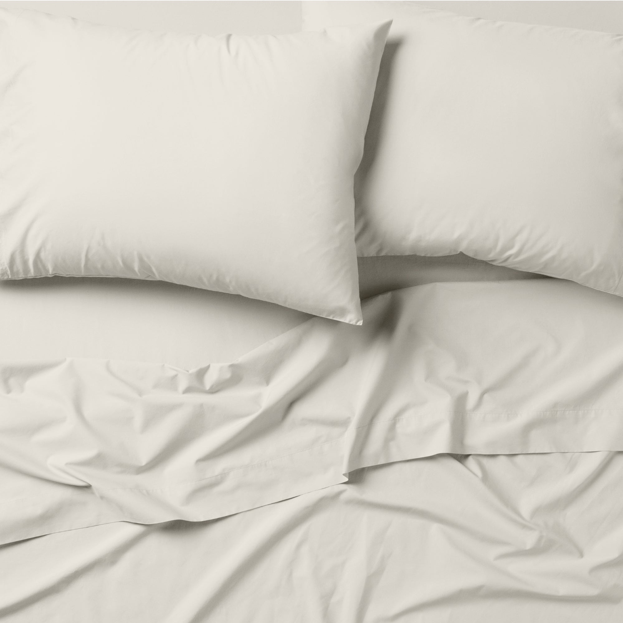 The Tuft and Needle Classic Percale Pillowcase Set, 2 pillows in a pillowcase on top of a spread out sheet || color: Sand
