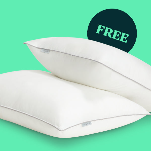 Two Tuft and Needle white rectangular pillows with piped edges shown on a bright mint green background, with a dark teal circular badge in the upper right containing the word "FREE" in light teal.