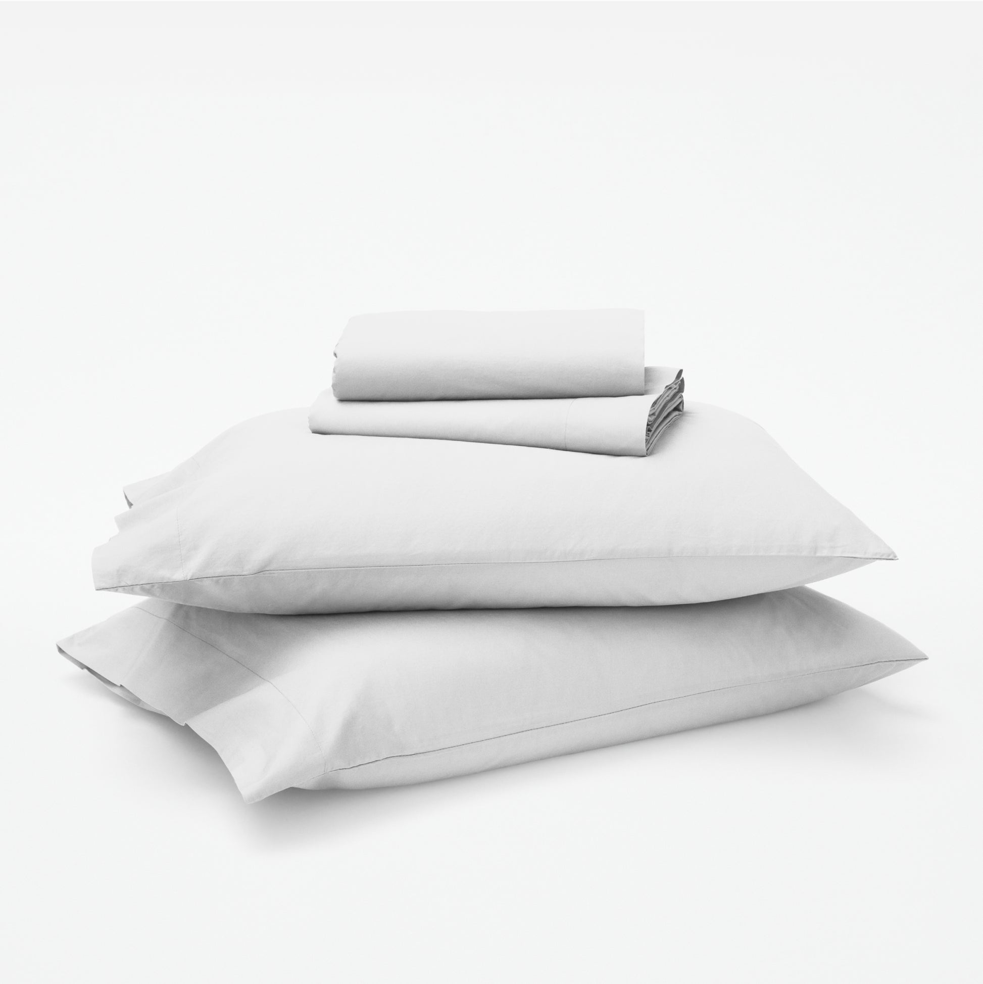 The Tuft and Needle Classic Percale Sheet Set, 1 sheet and pillowcases stacked on top of 2 pillows || color: Cloud