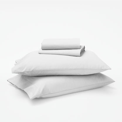 The Tuft and Needle Classic Percale Sheet Set, 1 sheet and pillowcases stacked on top of 2 pillows || color: Cloud