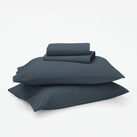 The Tuft and Needle Classic Percale Sheet Set, 1 sheet and pillowcases stacked on top of 2 pillows || color: Slate
