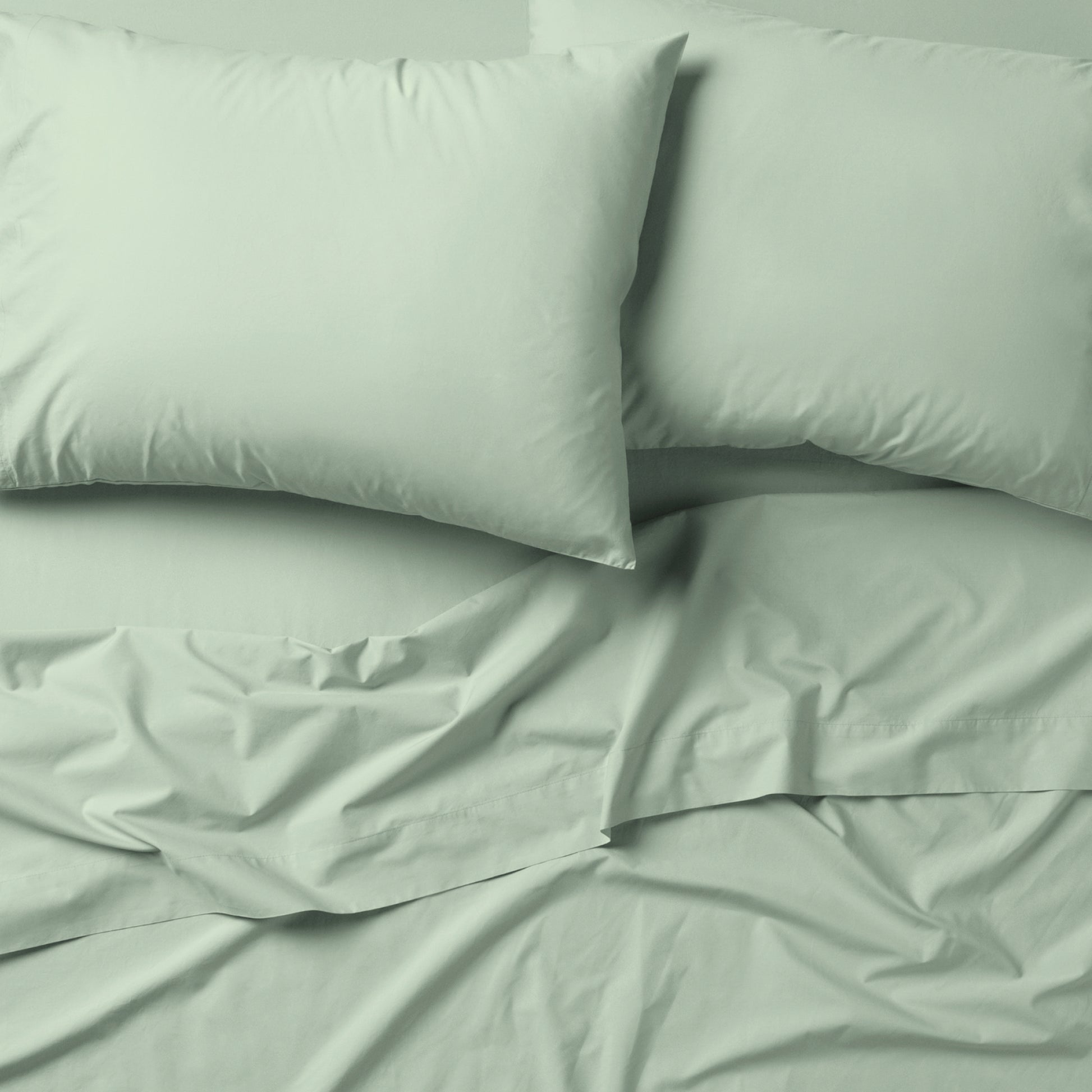 The Tuft and Needle Classic Percale Sheet Set, 2 pillows on top of a sheet on a mattress || color: Sage
