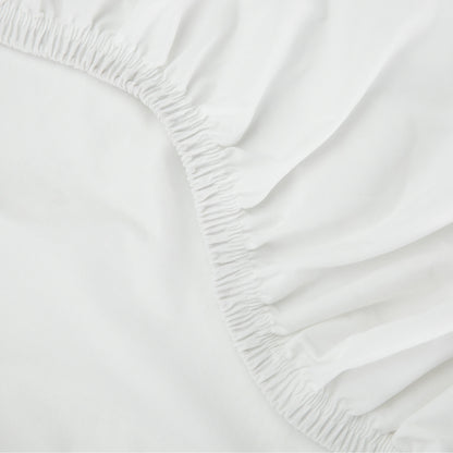  Close-up of a Tuft & Needle white fitted sheet with elastic waistband on a bed.