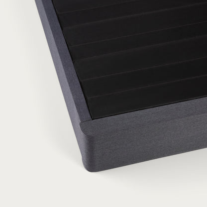 Corner of a Tuft & Needle black colored mattress foundation on a white background