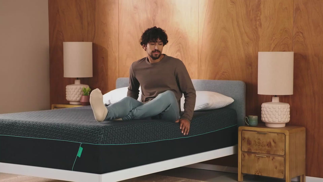Video of man sitting on a Tuft and Needle Mint Mattress sitting in a white bed frame.