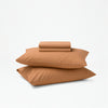 The Tuft and Needle Percale Sheet Set folded and stacked on 2 pillows||color:canyon