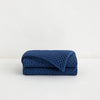 The Tuft and Needle Throw Blanket folded on a white background ||color:indigo